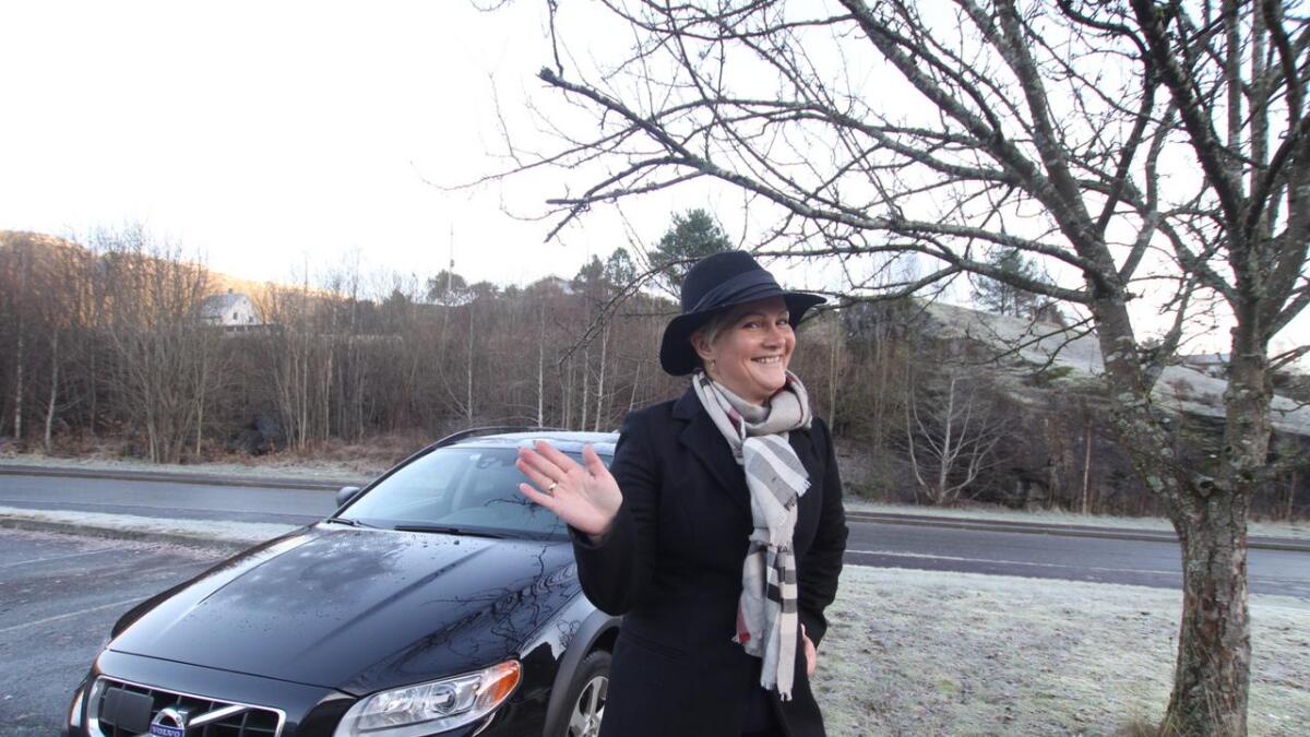 Anne Merete Hellebø har på seg hatt og vinkar pent når ho poserer framfor kongebilen.